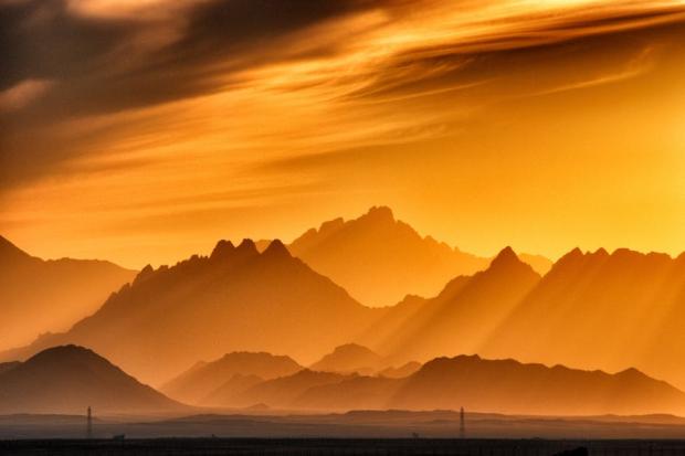 Breathtaking view of sunset casting silhouettes over Egyptian desert mountains in warm hues.
